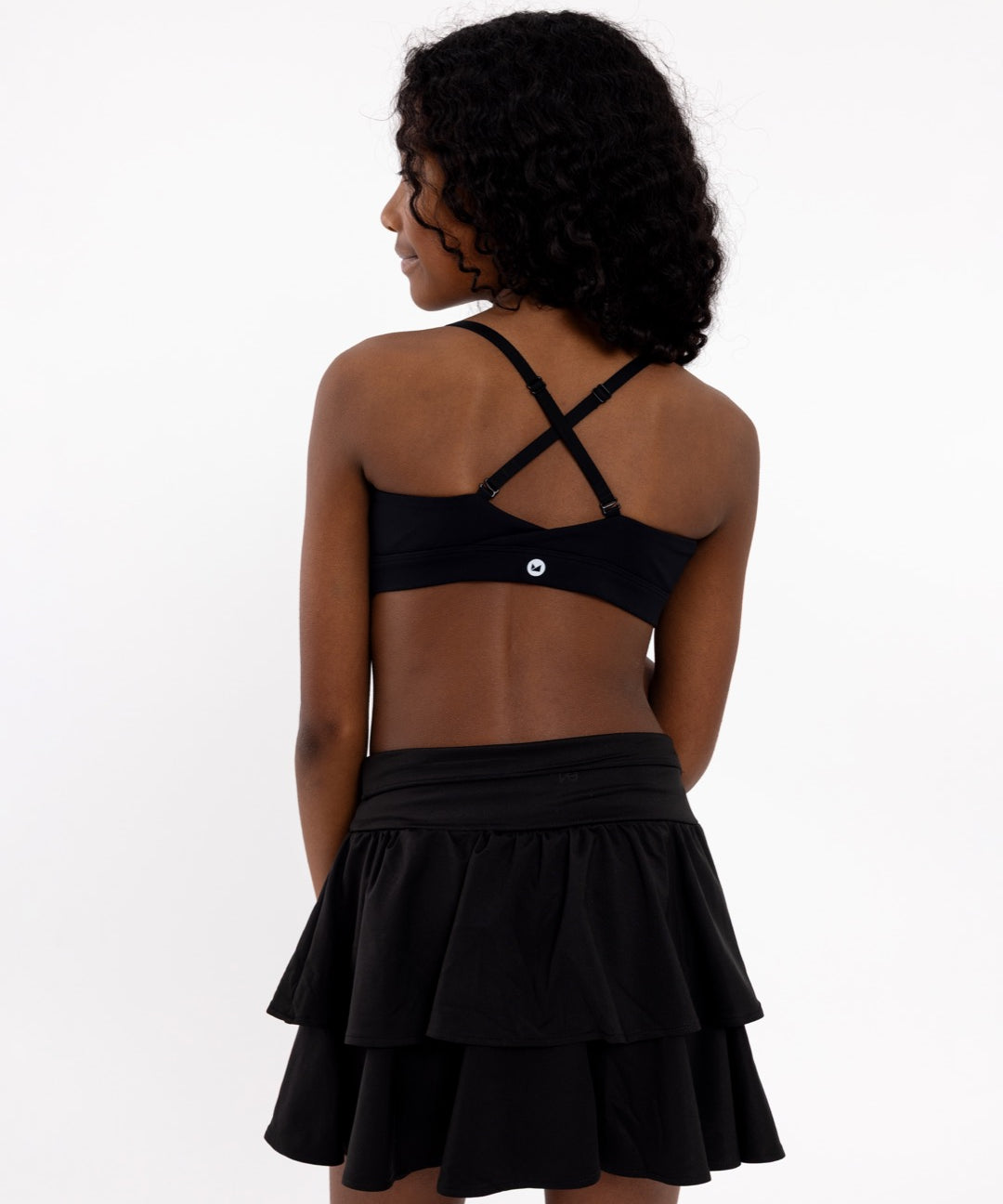 Close-up back view of a black SASSH Active sports bra for girls showing crossover racerback strap detail — seamless girls sports bra.
