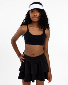 Girl wearing a black SASSH Active sports bra in a complete outfit on a white background — tween girls sports bra.