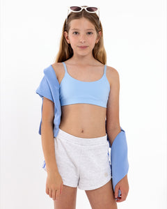 Girl wearing a light blue SASSH Active sports bra in a complete outfit on a white background — tween girls sports bra.