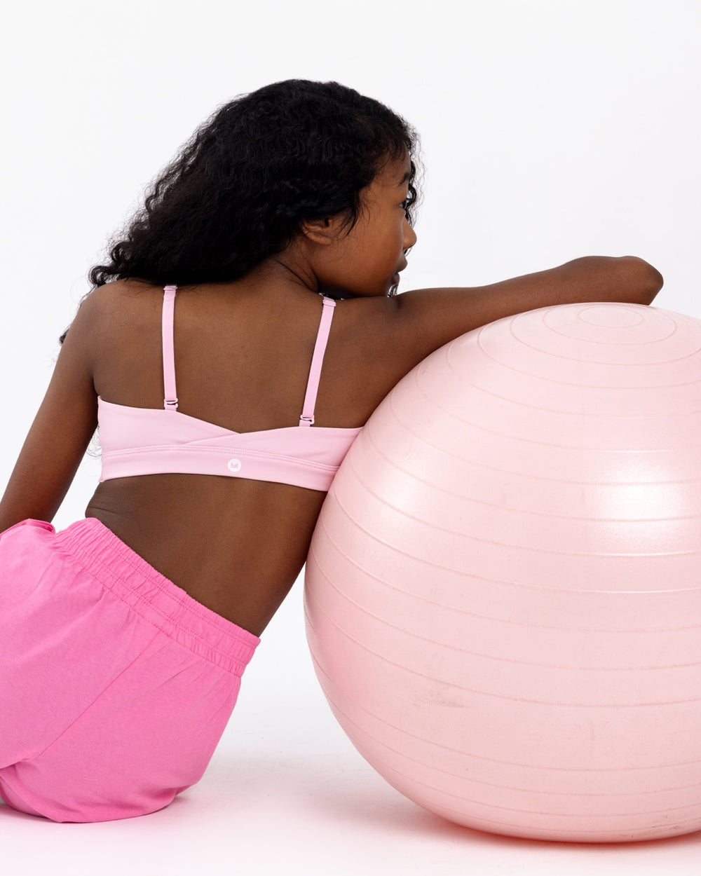 Back view of a girl wearing a pink SASSH Active sports bra for tweens, showing crossover racerback strap detail — girls sports bra.