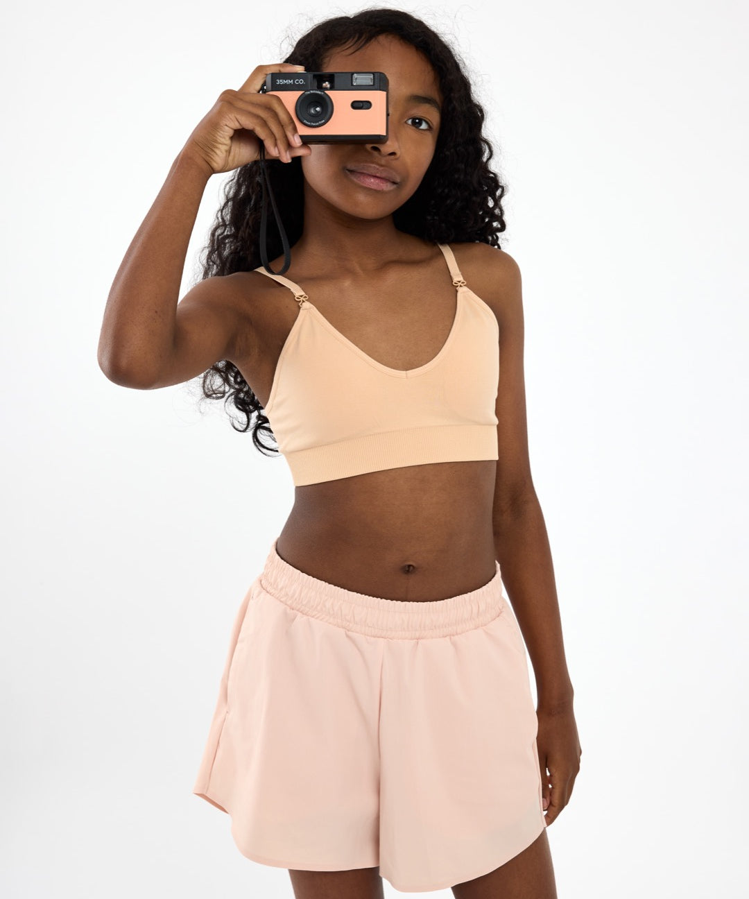 Girl wearing a beige SASSH Essential training bra in a complete outfit — seamless first bra for tweens and teens.
