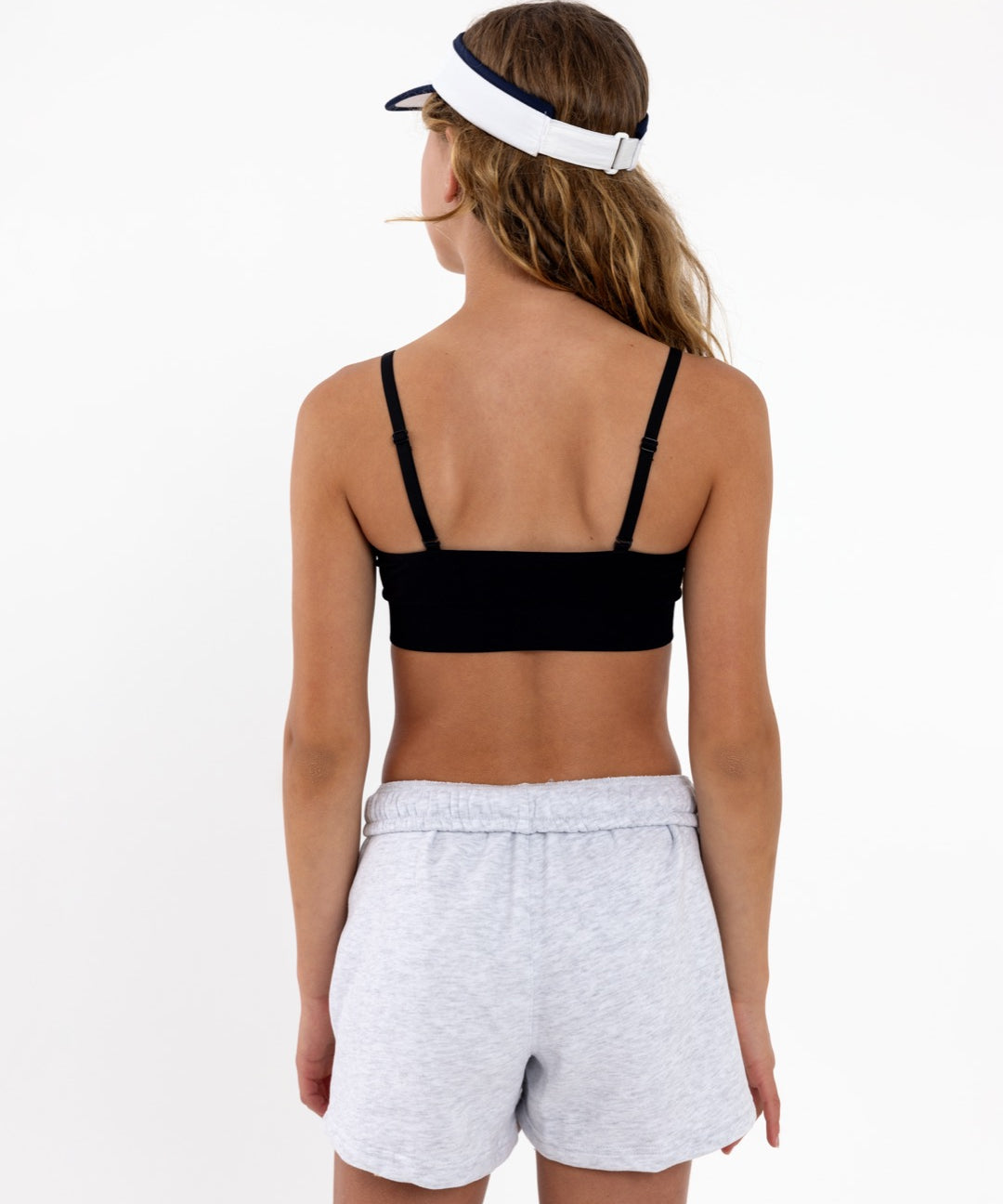 Back view of a girl wearing a black SASSH Essential training bra showing adjustable criss-cross straps — girls first bra, seamless training bra.