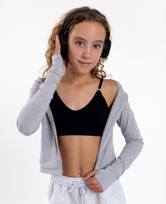 Girl wearing a black SASSH Essential training bra, front view, V-neck triangle style with adjustable straps and bow detail — girls first bra.