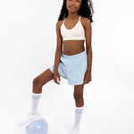 Girl wearing a white SASSH Essential training bra, front view, V-neck triangle style with adjustable straps and bow detail — girls first bra.
