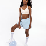 Girl wearing a white SASSH Essential training bra, front view, V-neck triangle style with adjustable straps and bow detail — girls first bra.
