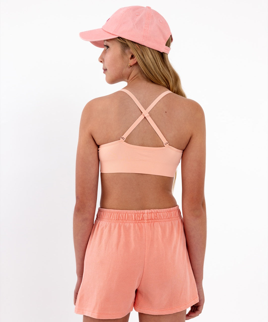 Close-up back view of a peach SASSH Essential training bra showing adjustable criss-cross straps and seamless underband — girls first bra.