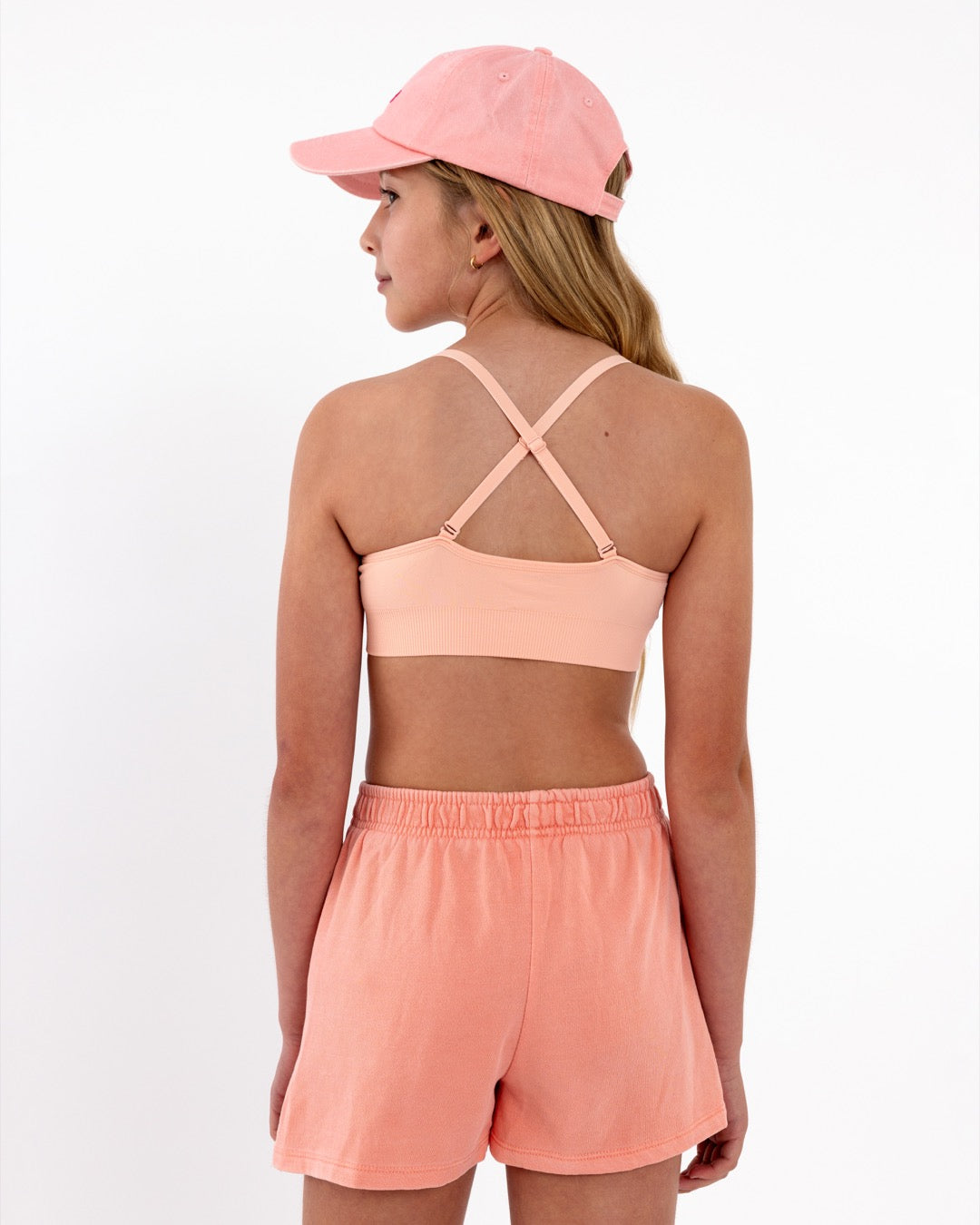 Close-up back view of a peach SASSH Essential training bra showing adjustable criss-cross straps and seamless underband — girls first bra.