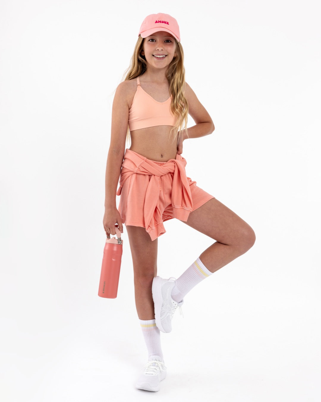 Girl wearing a peach SASSH Essential training bra in a complete outfit — seamless first bra for tweens and teens.