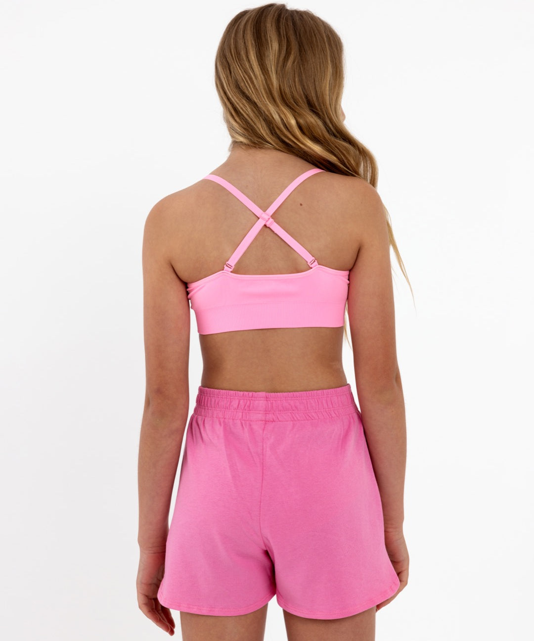 Back view of a girl wearing a bright pink SASSH Essential training bra showing adjustable criss-cross straps — girls first bra, seamless training bra.