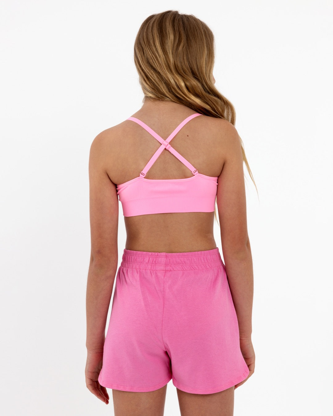 Back view of a girl wearing a bright pink SASSH Essential training bra showing adjustable criss-cross straps — girls first bra, seamless training bra.
