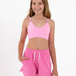 Girl wearing a bright pink SASSH Essential training bra, front view, V-neck triangle style with adjustable straps and bow detail — girls first bra.