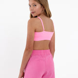 Side view of a girl wearing a bright pink SASSH Essential training bra showing seamless crop top fit — girls training bra, first bra.