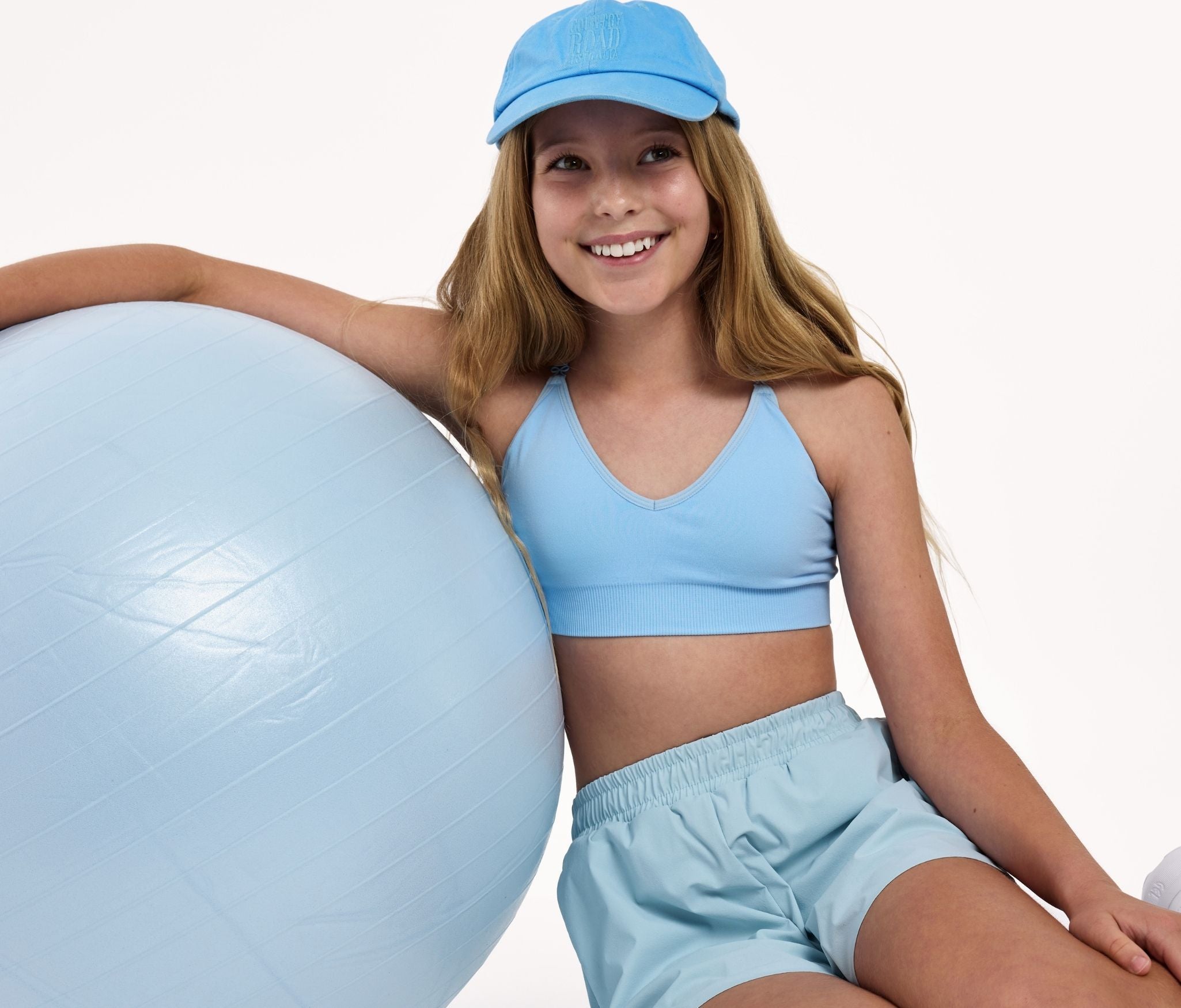 An 11 year old girl in light blue bra and outfit with a large exercise ball on a white background