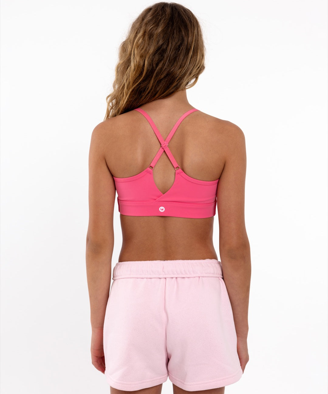 Back view of a girl wearing a hot pink SASSH The Energy sports bra showing crossover racerback strap detail — girls sports bra.