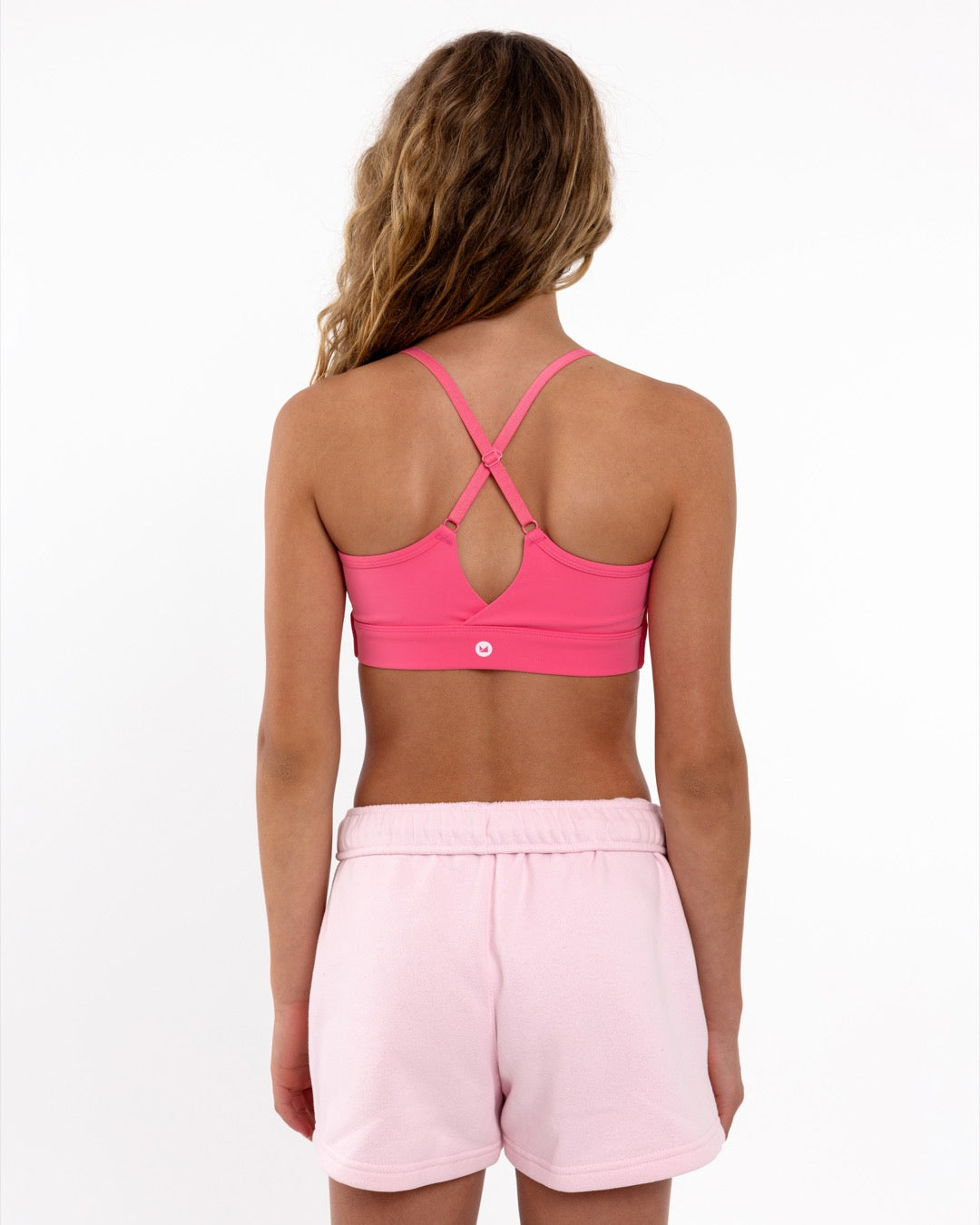 Back view of a girl wearing a hot pink SASSH The Energy sports bra showing crossover racerback strap detail — girls sports bra.