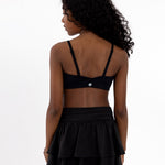 Back view of a girl wearing a black sports bra and skirt in a white background.