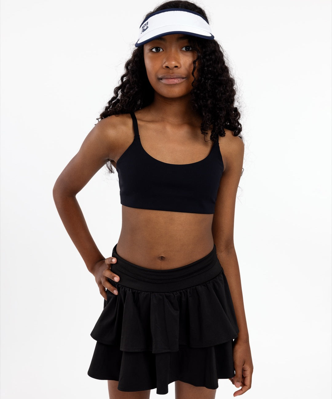 An 11-year-old girl wearing a black sports bra and skirt with a white visor on a white background.