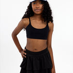 An 11-year-old girl wearing a black sports bra and skirt with a white visor on a white background.