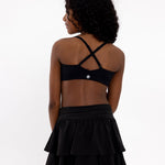 Back view of a girl wearing a black sports bra showing crossover detail, adjustable straps and a pullover style in a white background.