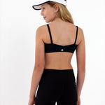 A tween girl wearing a black sports bra and shorts with a white visor on a white background.