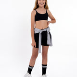 Girl wearing a black sports bra and shorts with a grey jacket wrapping around the waist in a white background.