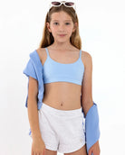Girl wearing a light blue first sports bra with a scoop neckline, adjustable straps, and a pullover style.