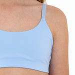 Close-up of a girl wearing a light blue sports bra in a white background.