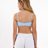 Back view of a girl wearing a light blue sports bra showing crossover detail, adjustable straps and a pullover style in a white background.