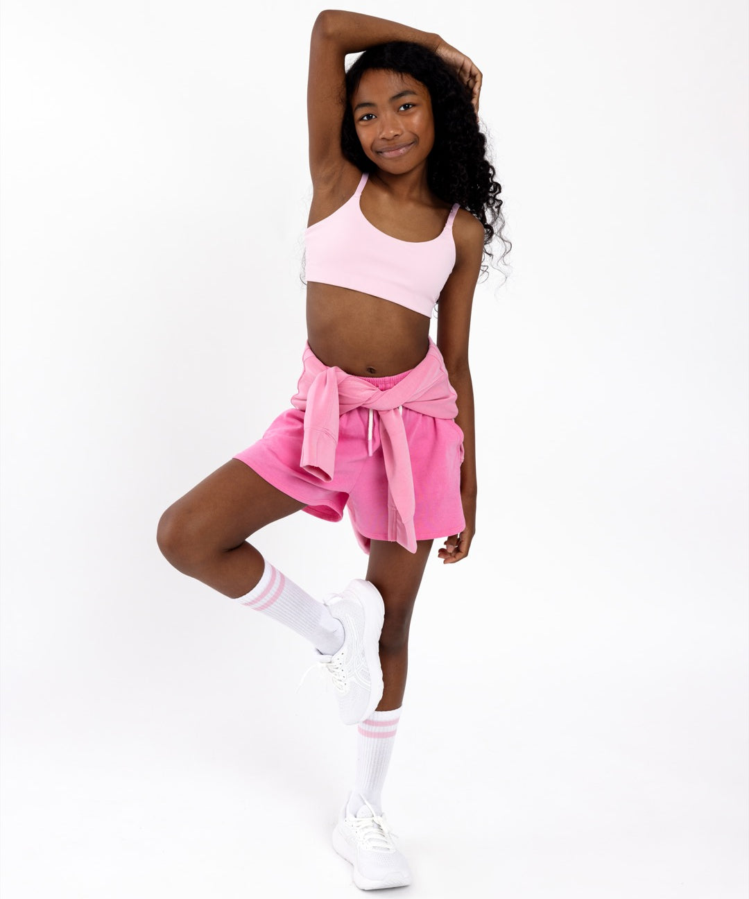 Girl wearing a pink sports bra with pink short on a white background.