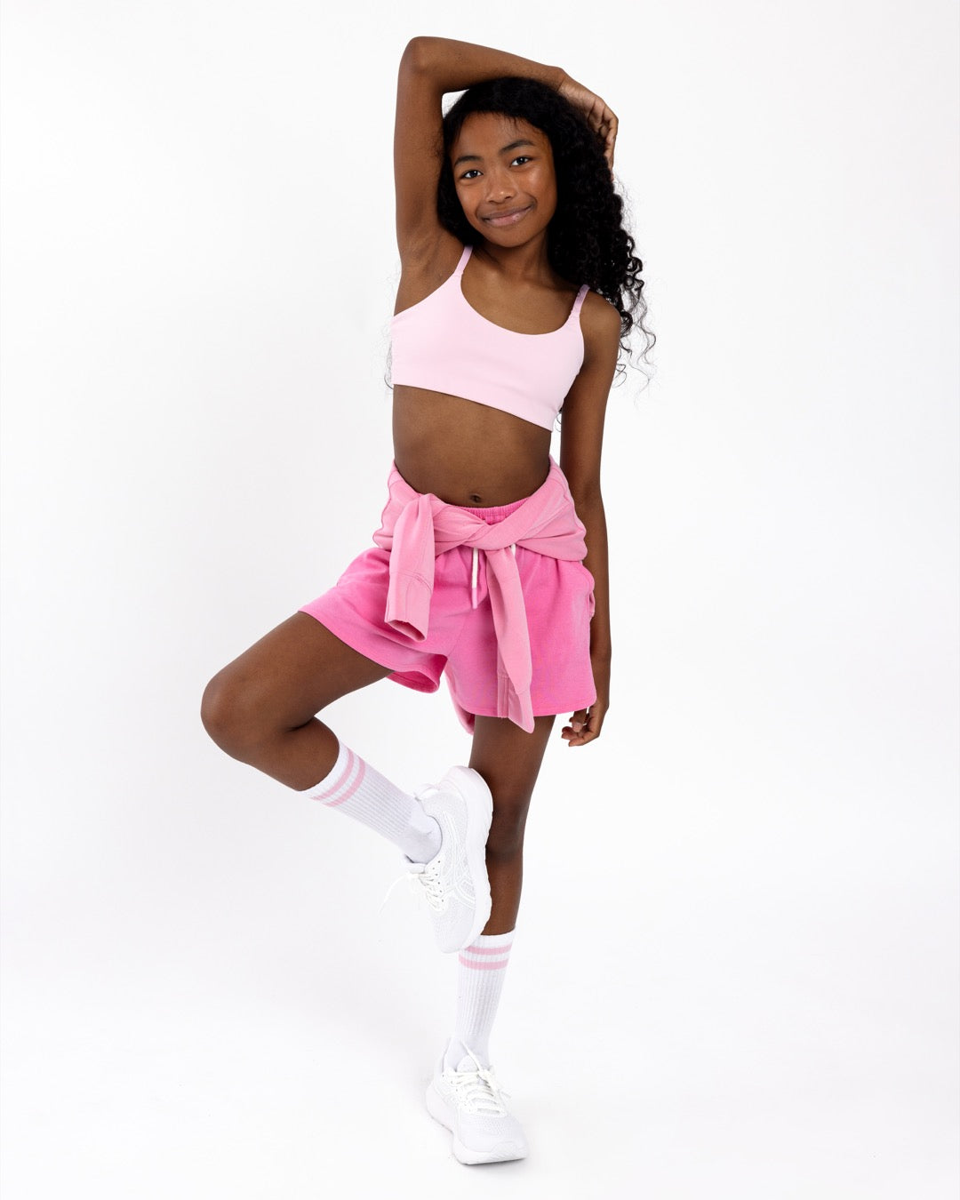 Girl wearing a pink sports bra with pink short on a white background.