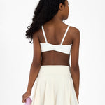 Back view of a girl wearing a white sports bra, holding a pink jacket on a white background.