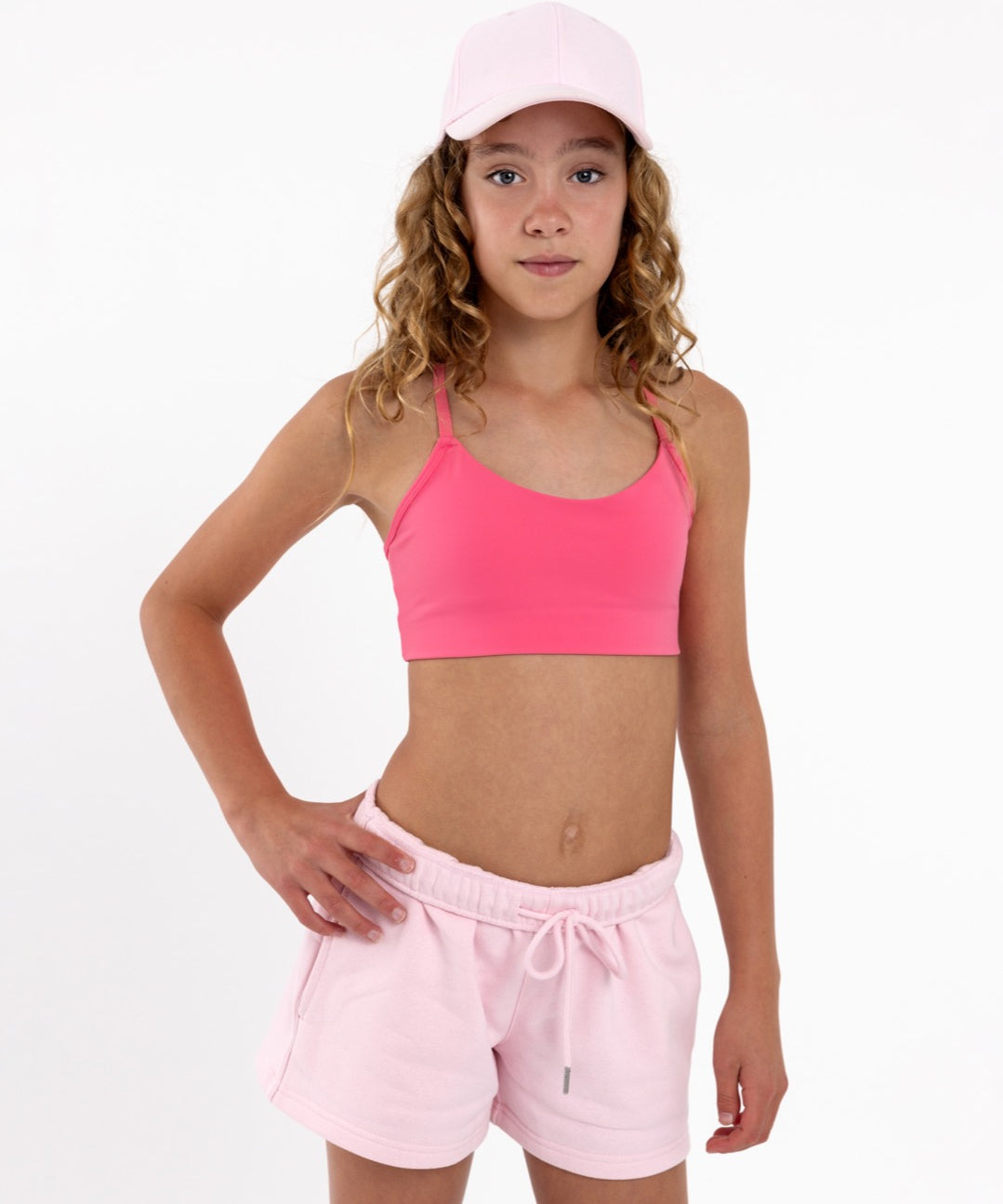 Girl wearing a hot pink girls sports bra showing smooth scoop neckline and a seamless underband on a white background.