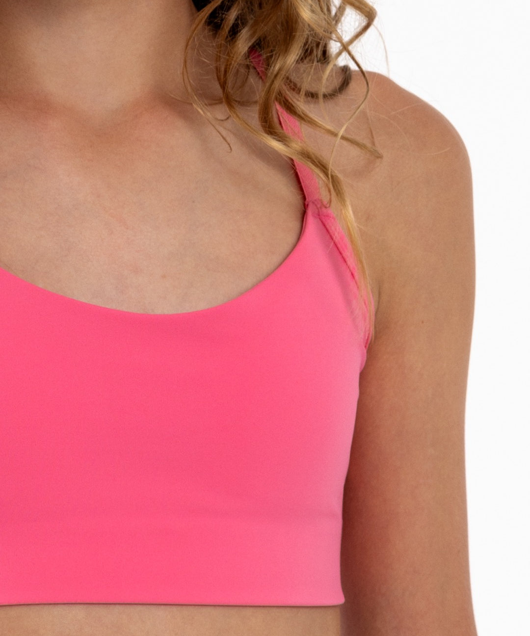 Close-up of a girl wearing a hot pink longline sports bra showing scoop neckline, adjustable straps, and a seamless underband.