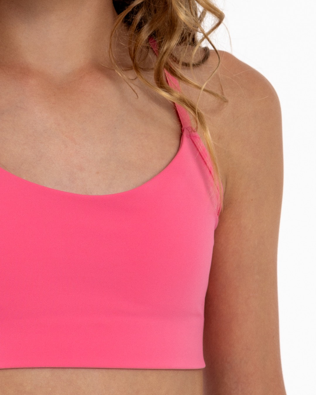 Close-up of a girl wearing a hot pink longline sports bra showing scoop neckline, adjustable straps, and a seamless underband.