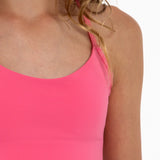 Close-up of a girl wearing a hot pink longline sports bra showing scoop neckline, adjustable straps, and a seamless underband.