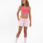 Girl wearing a hot pink longline sports bra showing smooth scoop neckline and a seamless underband on a white background.