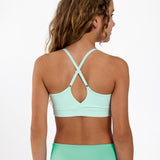 Back view of a girl wearing a mint green sports bra showing crossover racerback detail and adjustable straps.