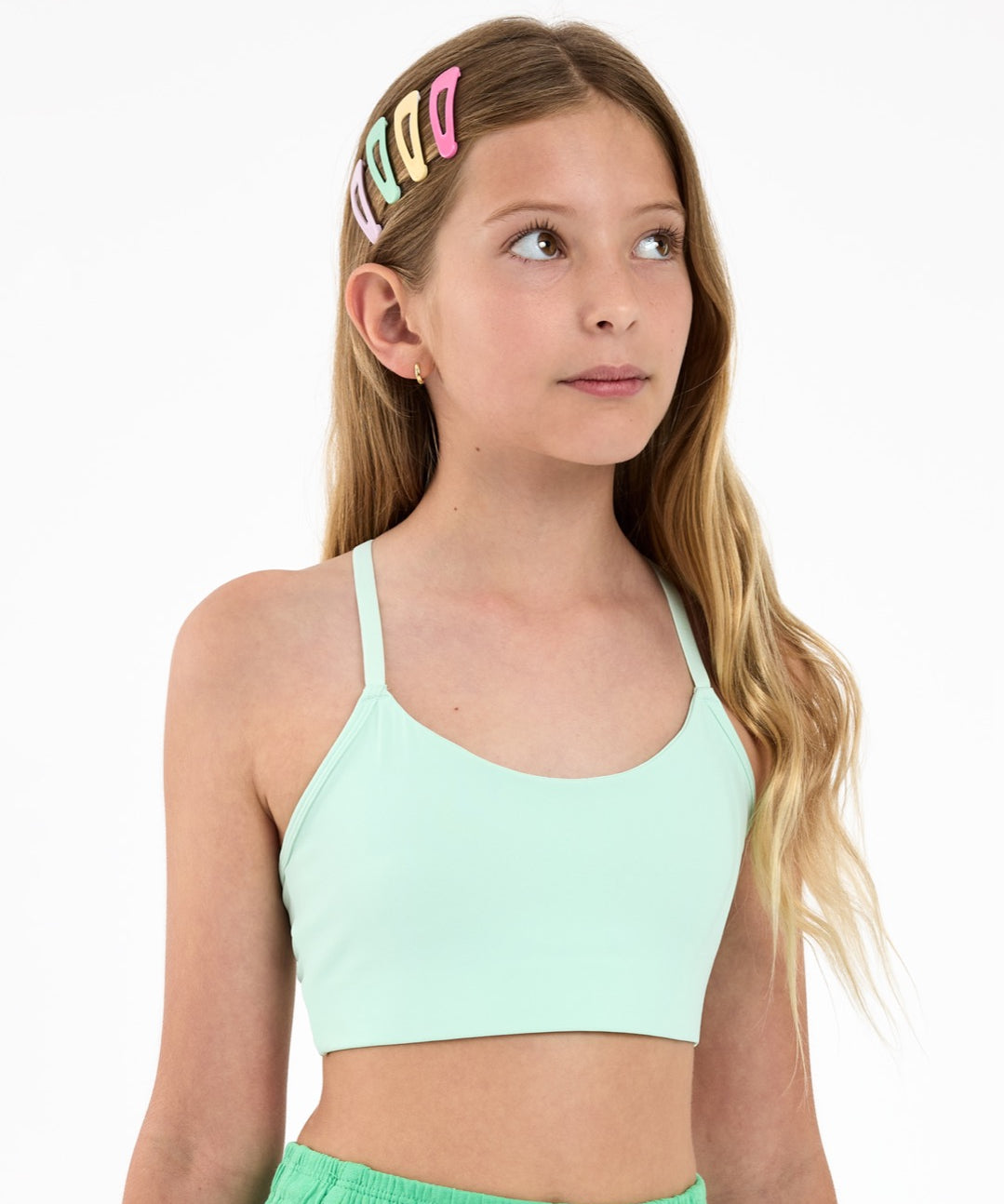 Girl wearing a mint green sports bra, with colourful hair clips  on a white background.