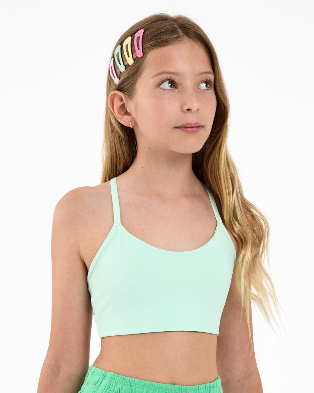 Girl wearing a mint green sports bra, with colourful hair clips  on a white background.