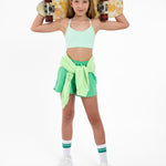Girl wearing a mint green sports bra and outfit holding a skateboard on a white background.