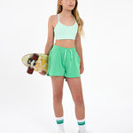Girl wearing a mint green sports bra and green outfit, holding a skateboard  on a white background.