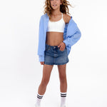 Girl wearing a white first sports bra and a denim skirt on a white background. 