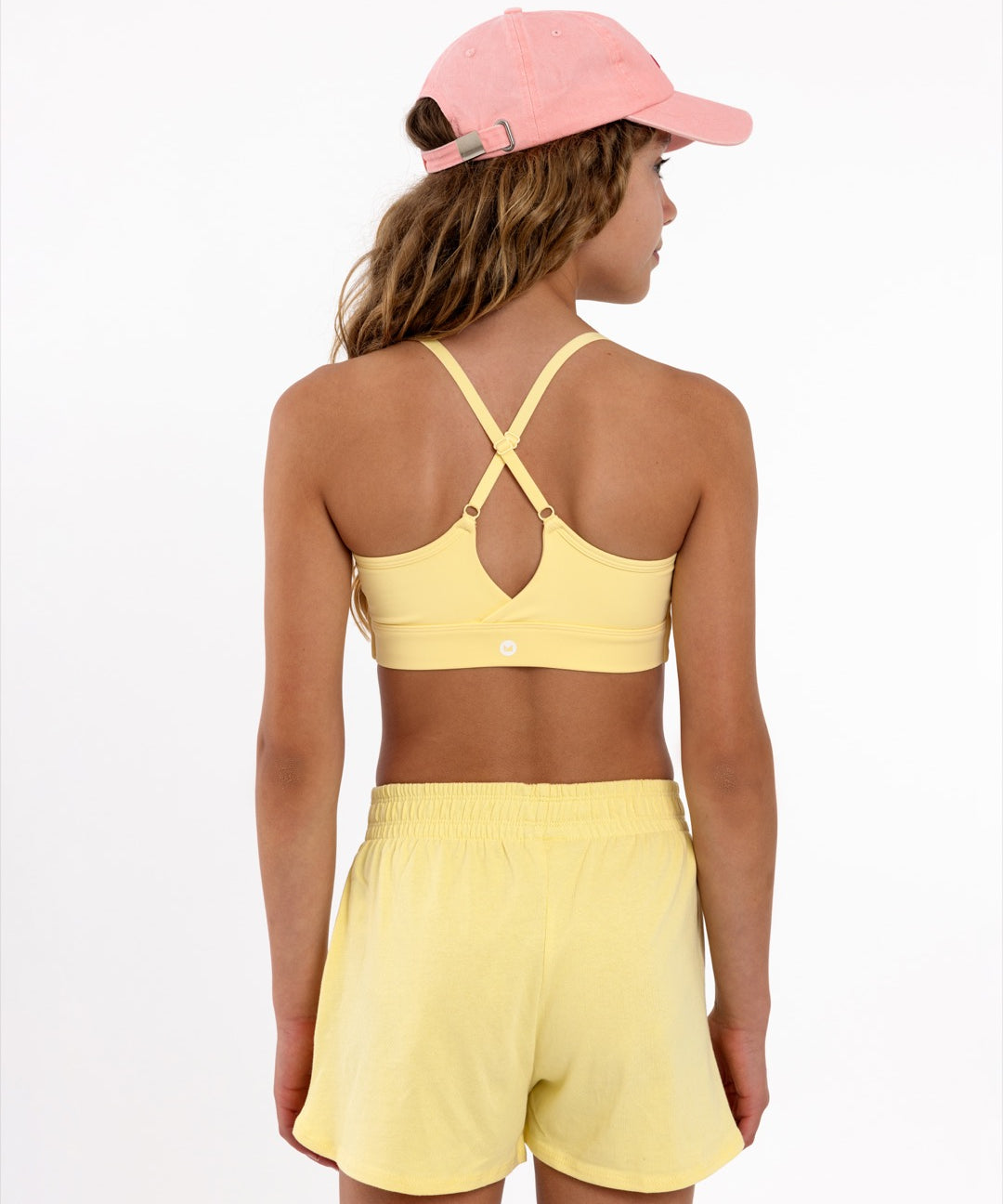 Back view of a girl wearing a yellow longline sports bra showing crossover racerback detail and adjustable straps on a white background.