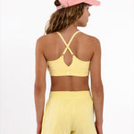 Back view of a girl wearing a yellow longline sports bra showing crossover racerback detail and adjustable straps on a white background.
