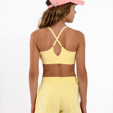 Back view of a girl wearing a yellow longline sports bra showing crossover racerback detail and adjustable straps on a white background.
