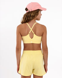 Back view of a girl wearing a yellow longline sports bra showing crossover racerback detail and adjustable straps on a white background.