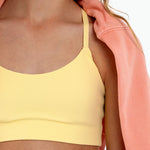 Close-up of a girl wearing a yellow longline sports bra showing scoop neckline, adjustable straps, and a seamless underband on a white background.