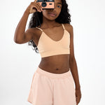 Girl holding a camera wearing a beige crop top training bra with a seamless underband and adjustable straps.