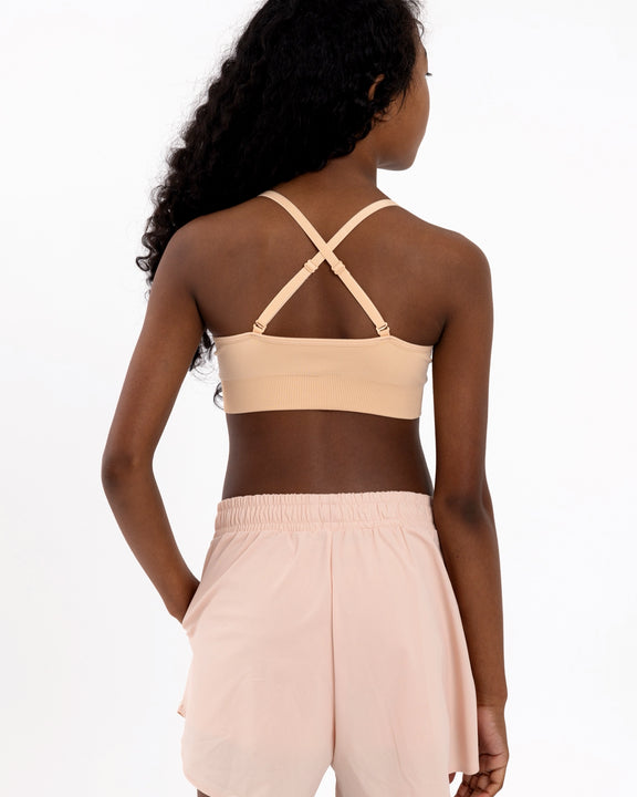 Back view of a girl wearing a beige first training bra showing adjustable crossover straps and seamless underband.