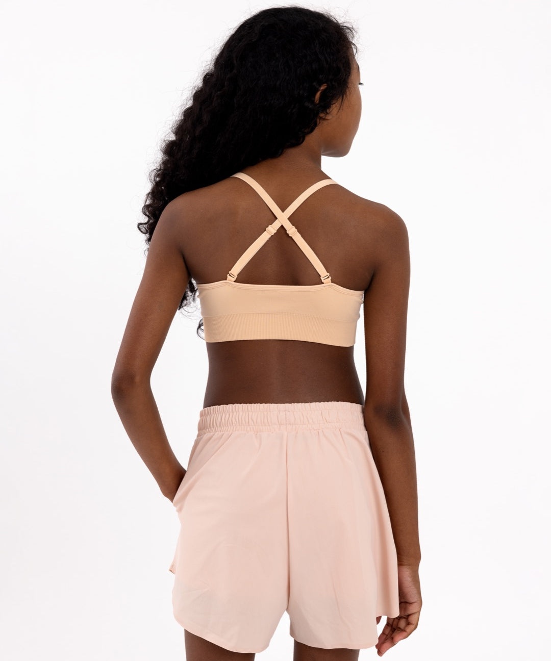 Back view of a girl wearing a beige first training bra showing adjustable crossover straps and seamless underband.